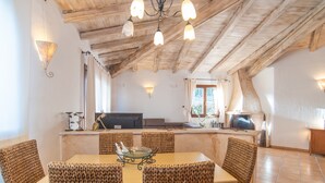 Un coin repas avec une table en bois et des chaises en osier, un lustre et une cuisine en arrière-plan.