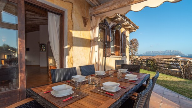 Un espace de restauration en plein air avec une table dressée pour six personnes, des chaises en osier et une vue sur le paysage.