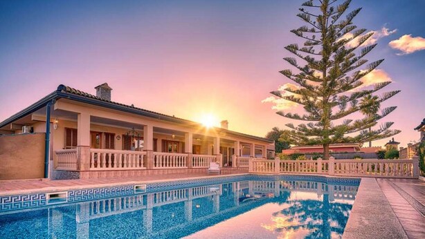 Un hotel con piscina, un árbol grande y una puesta de sol al fondo.