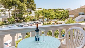 A balcony with a table, a bottle of wine, and a glass, overlooking a parking area and buildings. - Holiday Apartment "La Cabanya 2B" with Wi-Fi, balcony, terrace and shared pool (CANYAMEL)