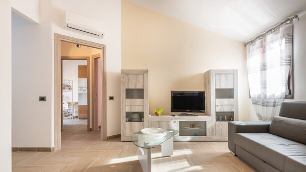Una sala de estar moderna con sofá, televisor y mesa de centro de vidrio.
