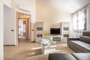 Ein modernes Wohnzimmer mit Sofa, Fernseher und Glastisch.