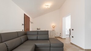 Una sala de estar moderna con un sofá modular, una mesa de centro de vidrio y una cocina al fondo.