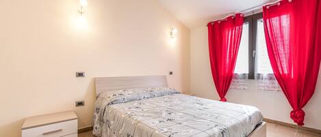 Een slaapkamer met een bed, een nachtkastje, een raam met rode gordijnen en wandlampen.