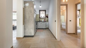 Un pasillo estrecho con una zona de cocina, suelo de baldosas y una puerta que da a otra habitación.