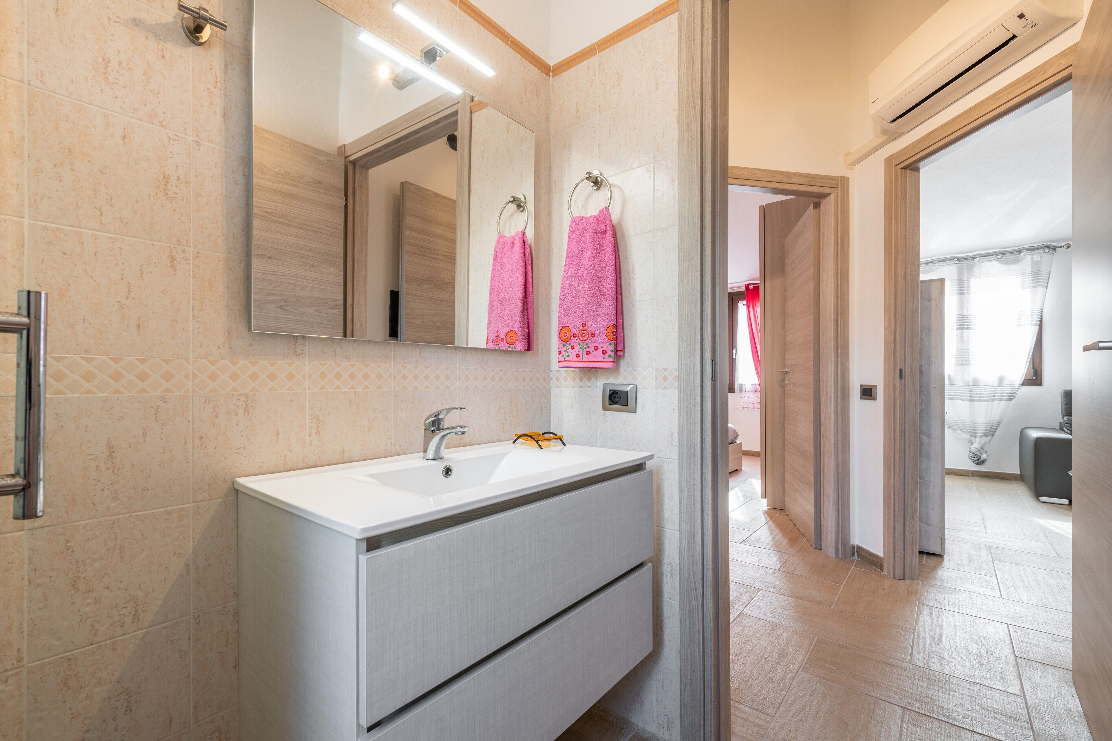 Une salle de bain avec un lavabo blanc, un miroir et deux serviettes roses suspendues à des crochets.