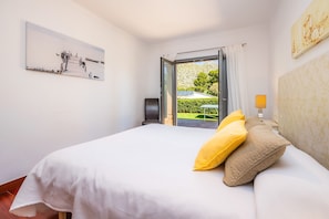 Une chambre à coucher avec un lit, un tableau, une lampe et une vue sur la verdure à l’extérieur.