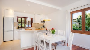 Une cuisine moderne avec des appareils électroménagers blancs, un coin repas avec des chaises blanches et une fenêtre donnant sur un paysage verdoyant.