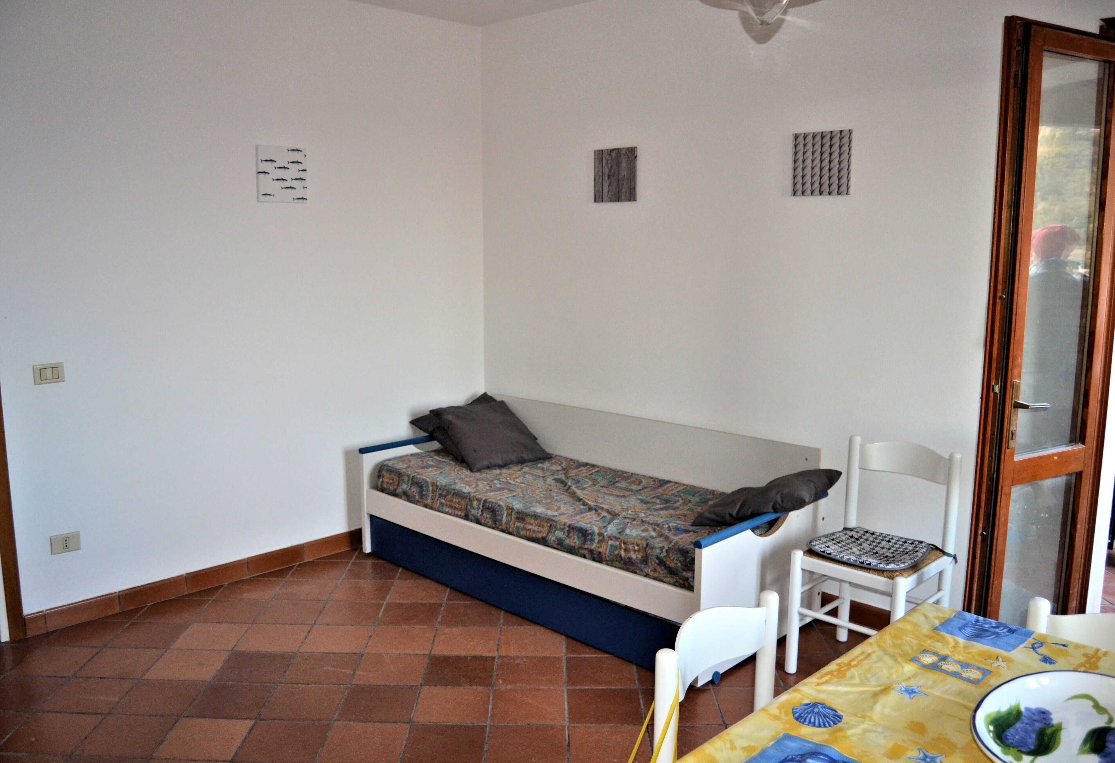 A small room with a single bed, a chair, a table, and a window.