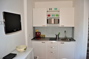 Une cuisine compacte avec des meubles blancs, un évier en acier inoxydable, une petite machine à café et un bol posé sur le comptoir.