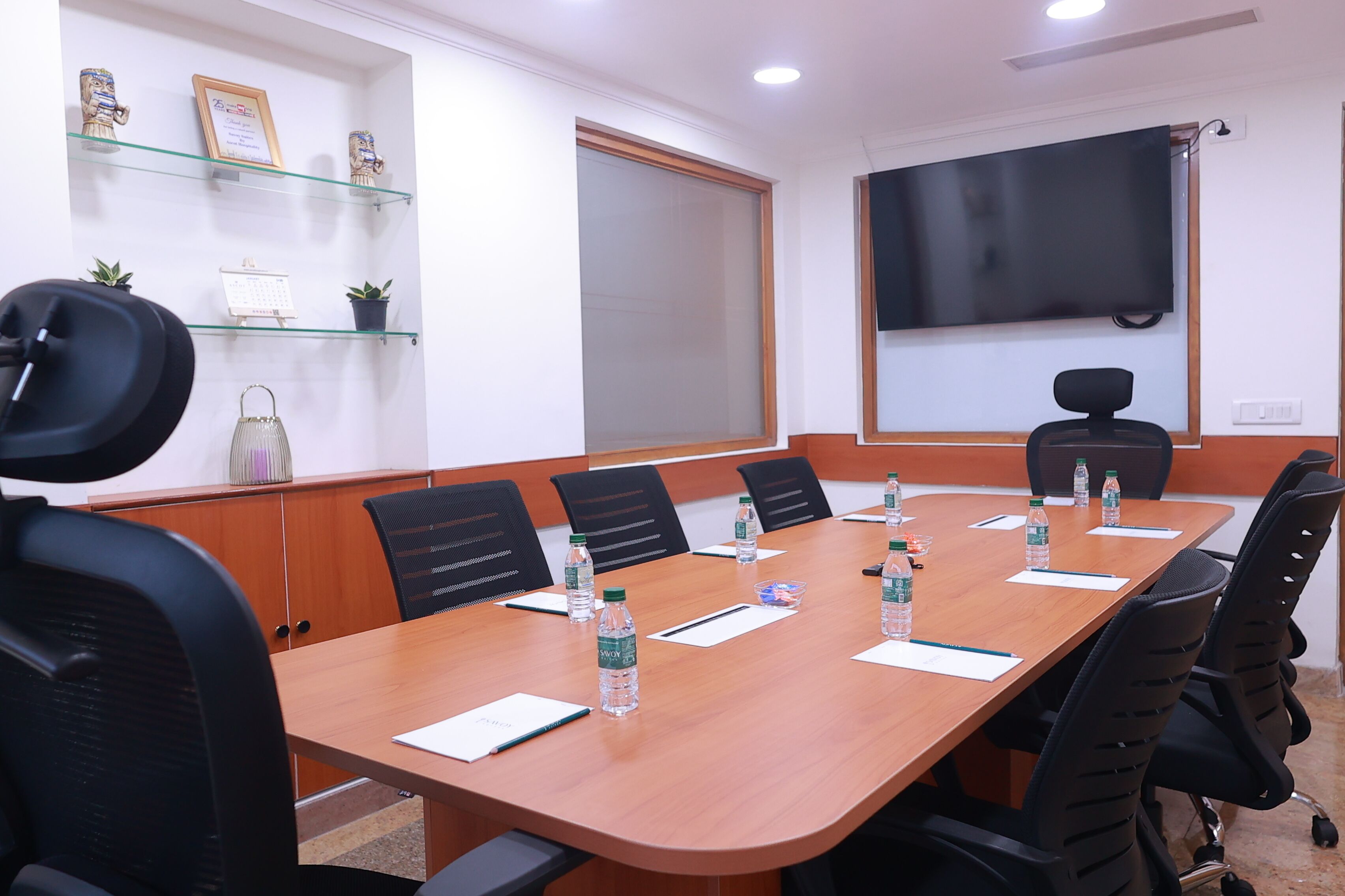 A conference room with a long table, black chairs, water bottles, and a TV screen on the wall.