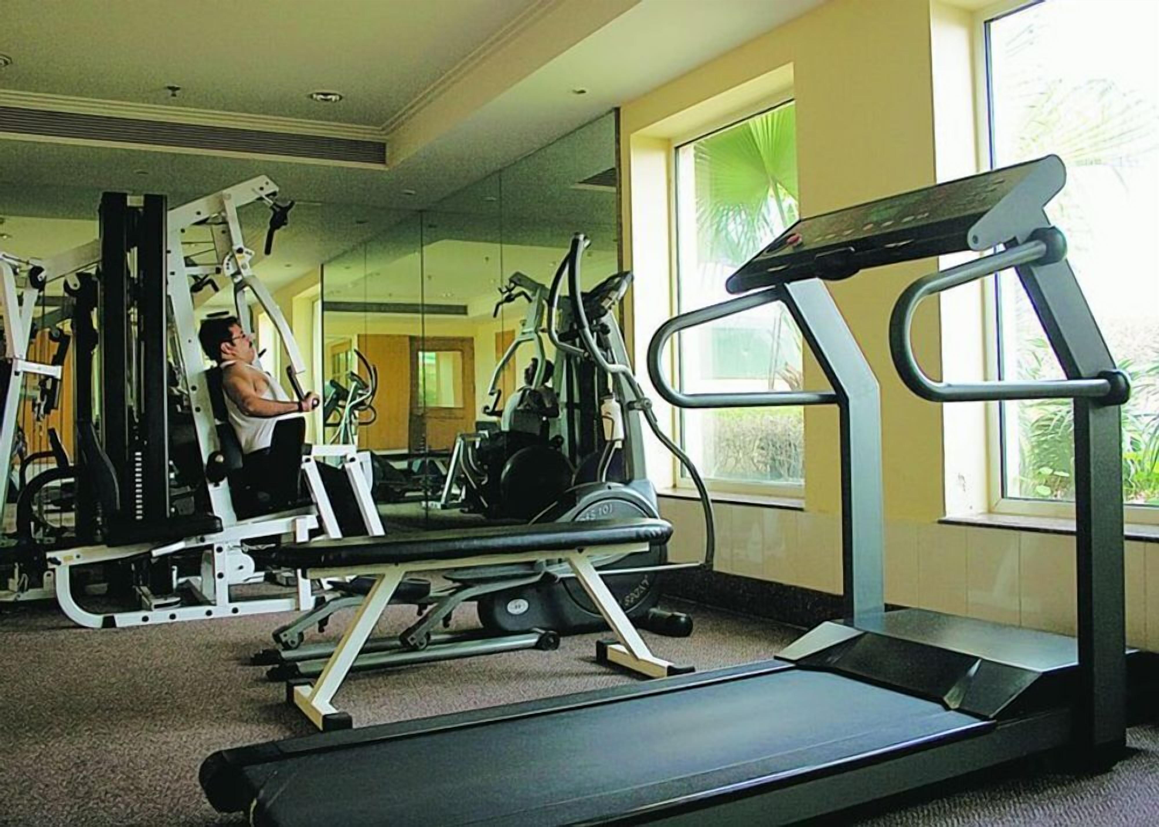 Une salle de sport équipée de matériel d’exercice, d’un tapis de course et d’un mur recouvert de miroirs.