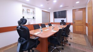 A conference room with a long table, black chairs, and a wooden door. - Savoy Suites Noida (Noida)