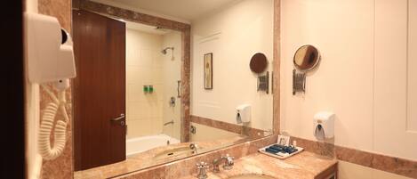 A bathroom with a marble sink, a large mirror, a handheld mirror, a towel dispenser, and a hand dryer.
