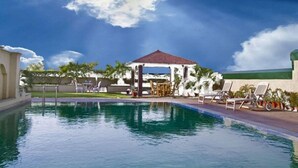 A pool area with lounge chairs, a gazebo, and palm trees. - Savoy Suites Noida (Noida)