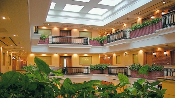 A multi-level atrium with a central open space, balconies with plants, and a high ceiling with skylights. - Savoy Suites Noida (Noida)