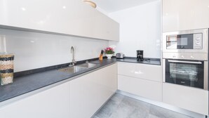 A modern kitchen with white cabinets, a black countertop, a stainless steel oven, and a sink.