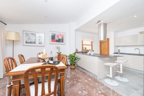 A modern kitchen with white cabinetry, a marble floor, and a dining area with wooden chairs and a table.