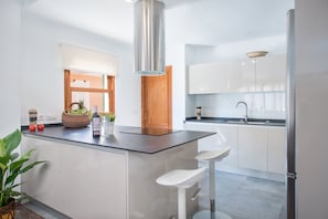 A modern kitchen with a central island, white cabinetry, a stainless steel range hood, and a built-in sink.