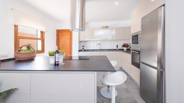 A modern kitchen with a stainless steel refrigerator, a central island with seating, and a large window.