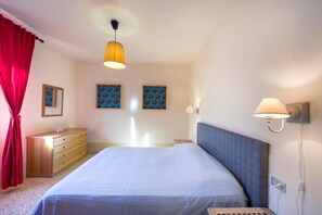 Ett sovrum med en säng, en byrå, ett sängbord och en vägglampa.