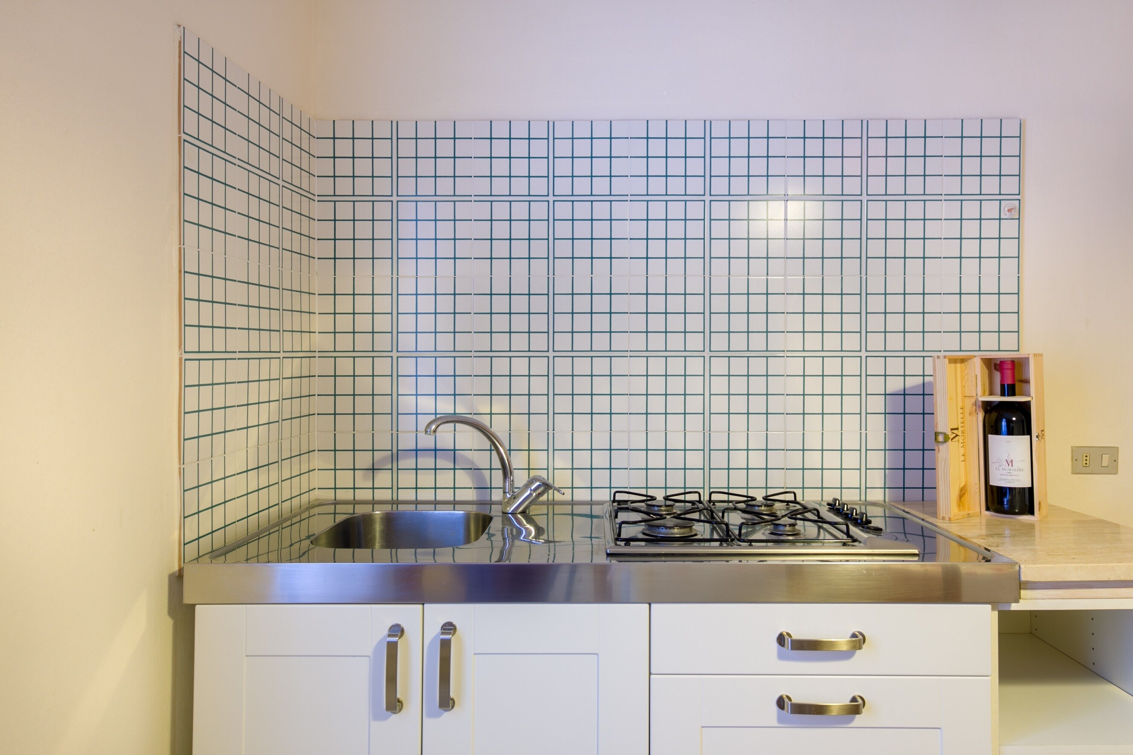 Cocina con salpicadero de diseño en cuadrícula, pileta de acero inoxidable, estufa a gas y alacenas blancas.