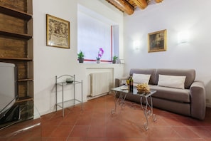 A living room with a sofa, a coffee table, a TV, a radiator, and a window with plants. - GuestHost - Jewish Ghetto ZTL Apartment x6! (Ferrara)