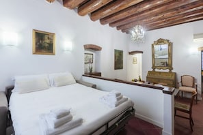 A bedroom with a bed, a wooden ceiling, a chandelier, a dresser, a chair, and wall-mounted artwork. - GuestHost - Jewish Ghetto ZTL Apartment x6! (Ferrara)