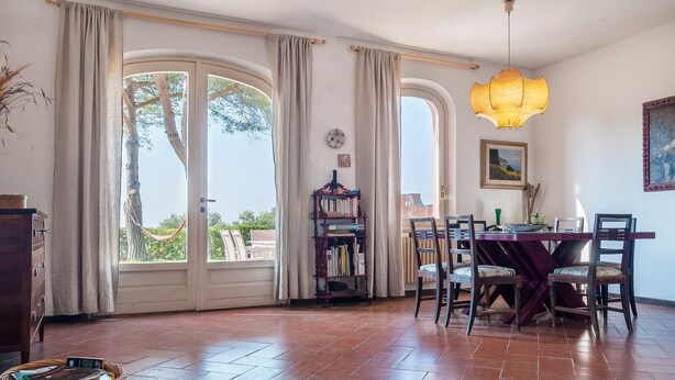 A dining area with a table, chairs, a bookshelf, and a large window with curtains.