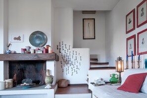 A room with a fireplace, wall-mounted keys, framed pictures, and a bed with a red pillow.