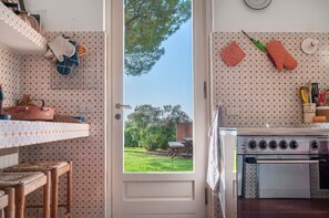 A kitchen with patterned wallpaper, a stove, and a door leading to a garden.