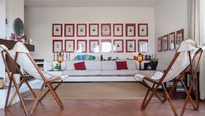 A living room with a white sofa, two wooden chairs, a coffee table, and framed pictures on the wall.