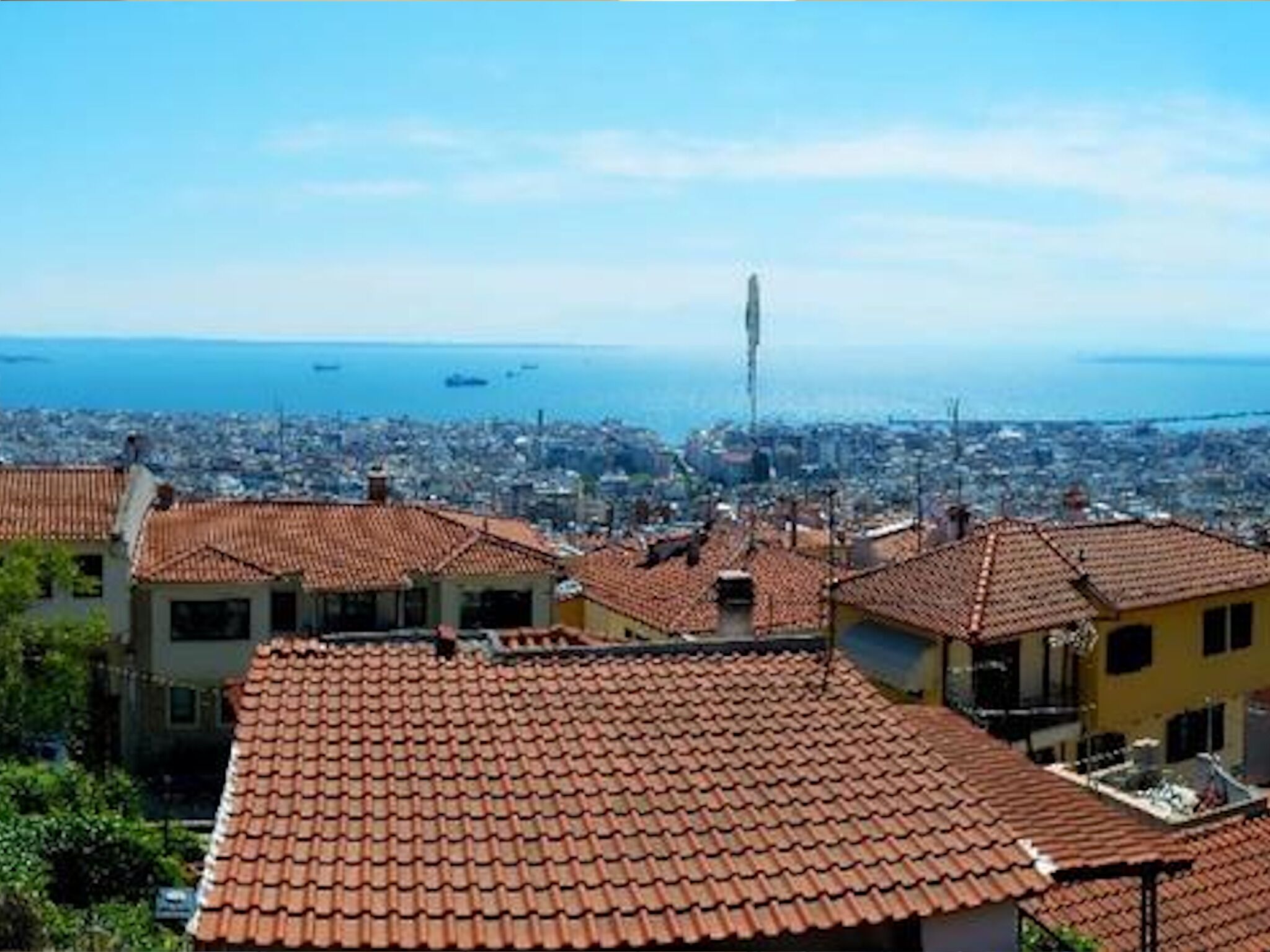 A coastal cityscape with terracotta-tiled rooftops, a prominent tower, and a view of the sea.
