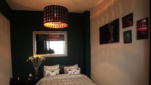 Ein Schlafzimmer mit Bett, Spiegel, Pendelleuchte und Wandbildern.