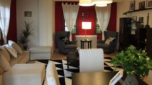 Ein Wohnzimmer mit Schachbrettmuster-Boden, zwei Sesseln, einem Sofa, einem Tisch und einer Lampe.