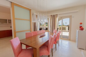 A dining area with a wooden table and pink chairs, a white cabinet, and a view through a glass door.