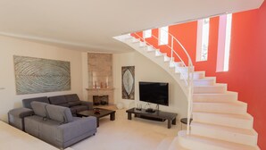 A modern living room with a sofa, coffee table, TV, fireplace, and a staircase with a red accent wall. - Stunning villa with pool & sea view – Villa Maitreya (san jaime, son bou, Alaior)