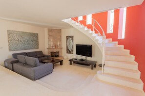 Una sala de estar moderna con sofá, mesa de centro, televisor, chimenea y una escalera con pared de acento roja.