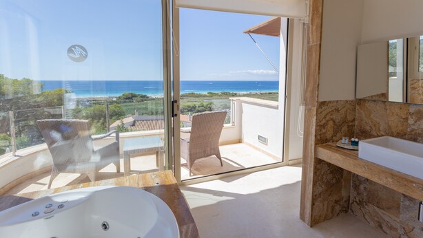 A balcony with a view of the ocean, a jacuzzi, a bathroom with a marble sink, and wicker furniture. - Stunning villa with pool & sea view – Villa Maitreya (san jaime, son bou, Alaior)