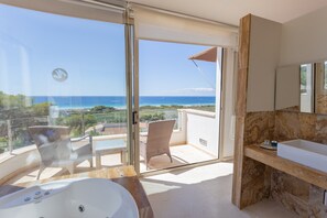 A balcony with a view of the ocean, a jacuzzi, a bathroom with a marble sink, and wicker furniture.