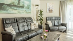 A living room with a sofa, a chair, a coffee table, and a painting of a lighthouse on the wall. - Wonderful Apartment in the house Seeblick (Salem)