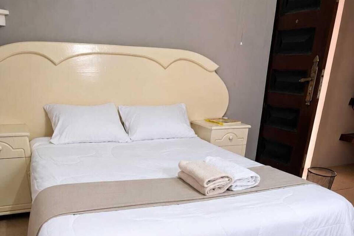 A double bed with white bedding, a beige headboard, and a nightstand with a lamp.