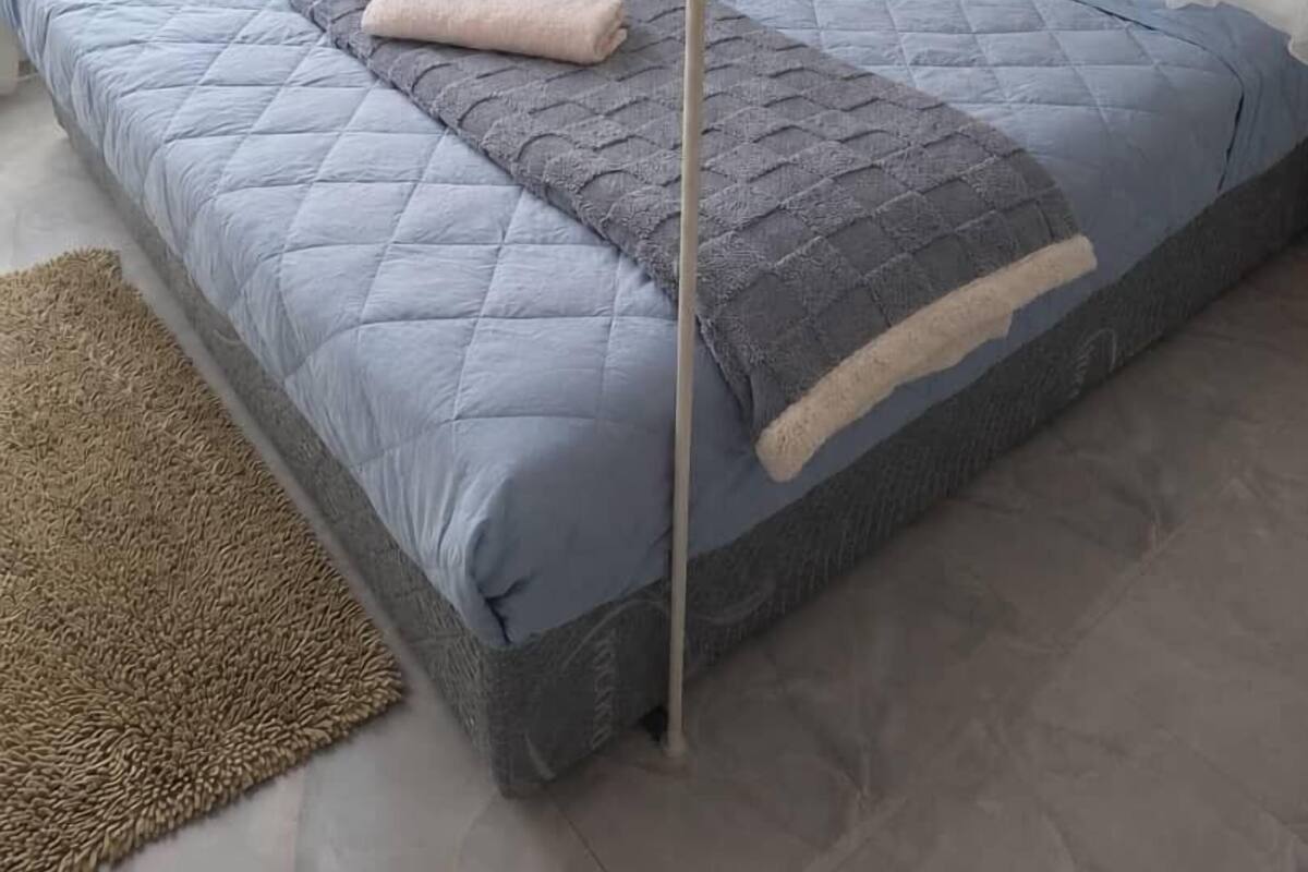A bed with a quilted blue cover, a grey blanket, and a beige pillow.