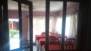 Una habitación con comedor que cuenta con mesas y sillas rojas, piso de baldosas y vista al exterior a través de un ventanal.