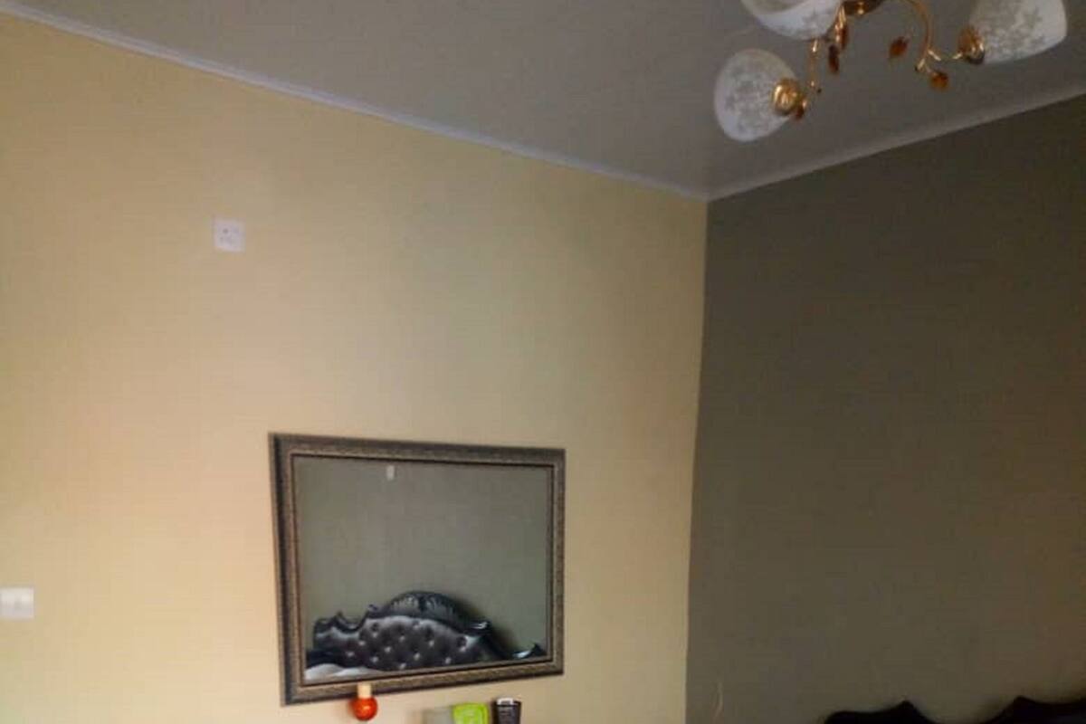 A bedroom with a bed, a dresser, a mirror, a small refrigerator, and a nightstand.