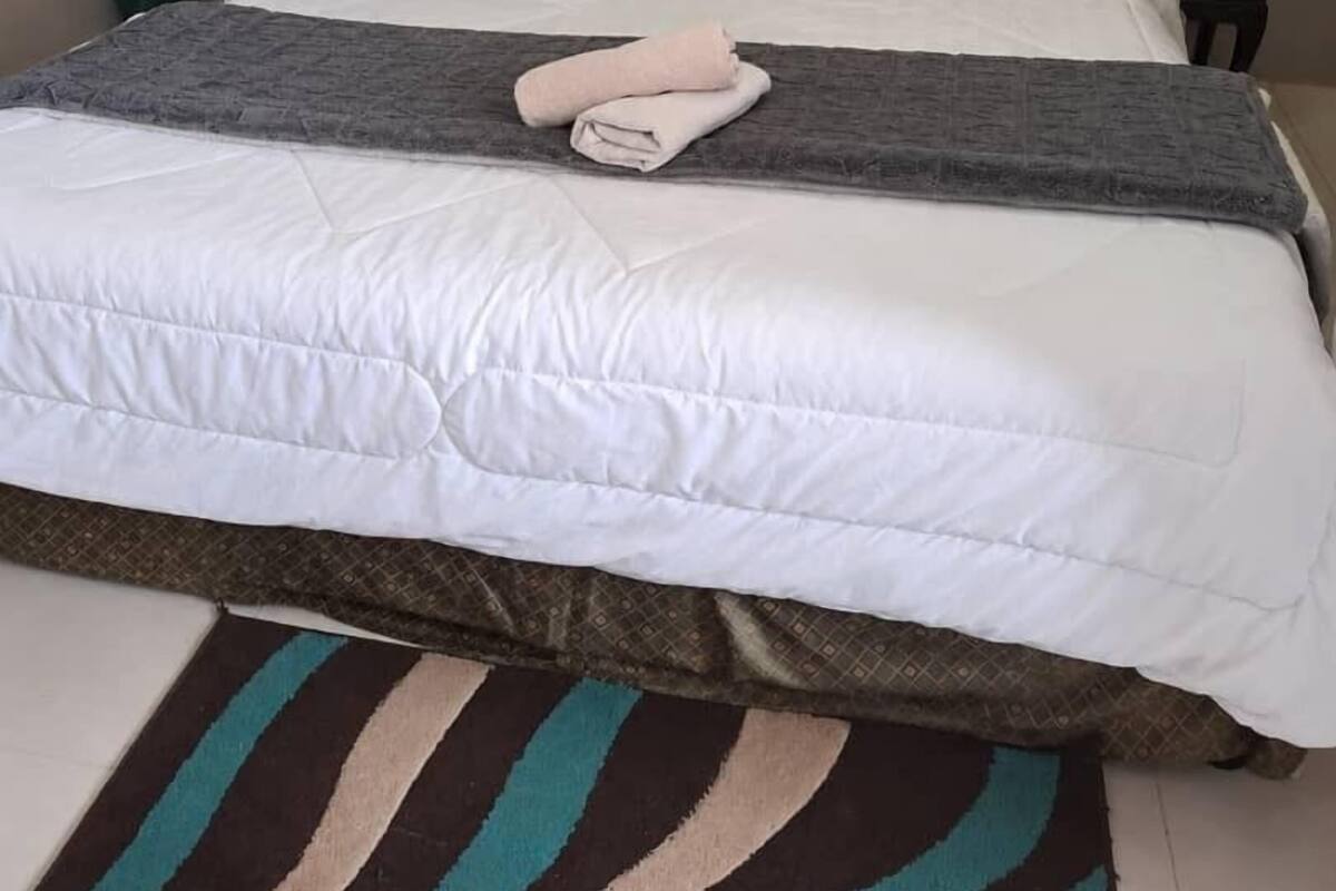 A neatly made bed with a white duvet, a grey blanket, and a rolled towel.