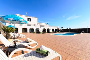 Un espace aménagé au bord de la piscine, avec des chaises longues, une piscine et un bâtiment doté de fenêtres en arc de cercle.
