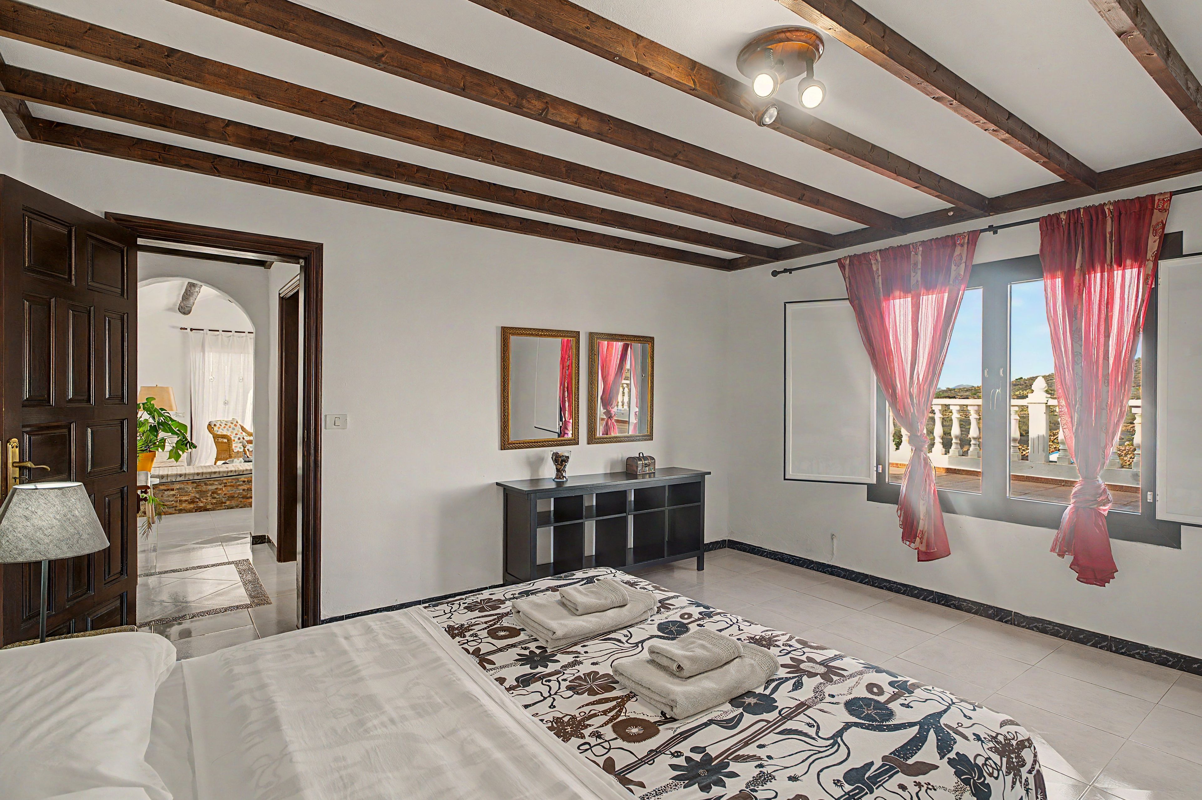 A hotel room with a bed, a console table, a mirror, and a window with curtains.