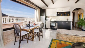 Une cuisine spacieuse avec des meubles blancs, un coin repas doté de chaises en osier et une vue sur la mer.