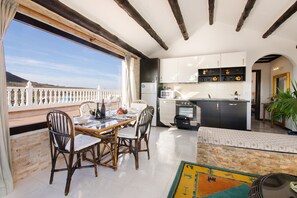 Une cuisine spacieuse avec des meubles blancs, un coin repas doté de chaises en osier et une vue sur la mer.